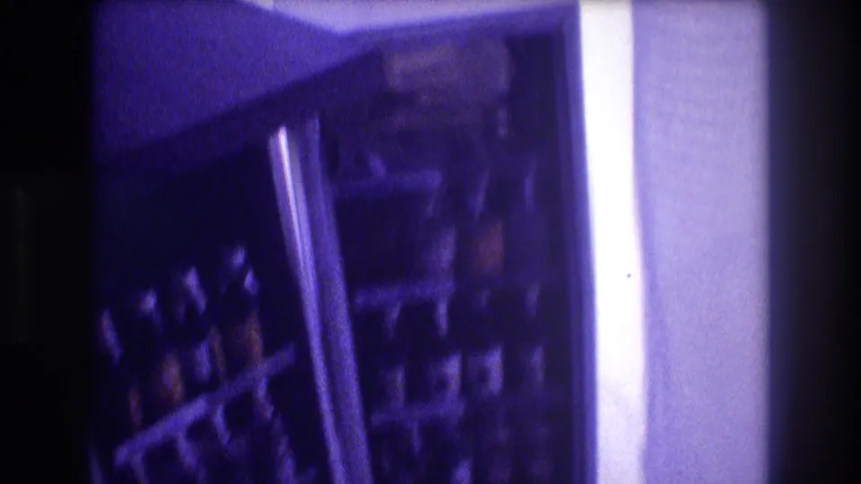 Handheld 8mm frame showing refrigerator door and interior shelves with bottles, motion blur and heavy purple cast, circa 1982.