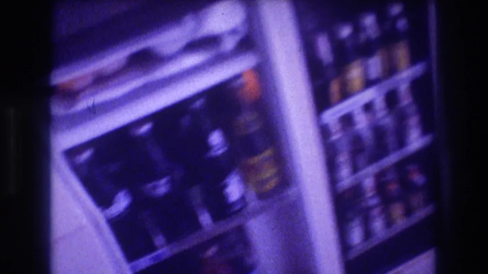 Open refrigerator in 1982 Acapulco home-movie footage with glass soda bottles, door storage, and visible branded labels under a purple film cast.