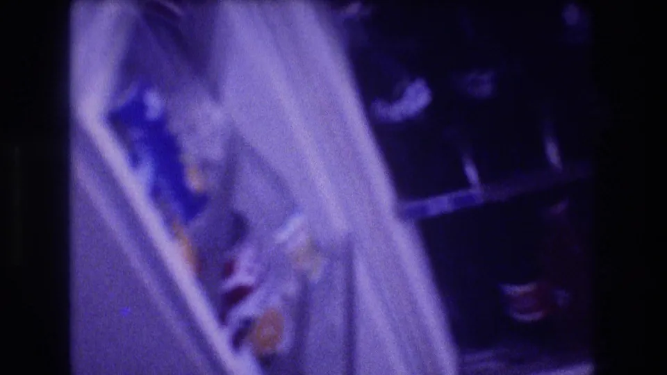 Blurred handheld frame from the 1982 Acapulco clip showing the open refrigerator door, stocked shelves, and dark soda bottles in purple-tinted 8mm film.