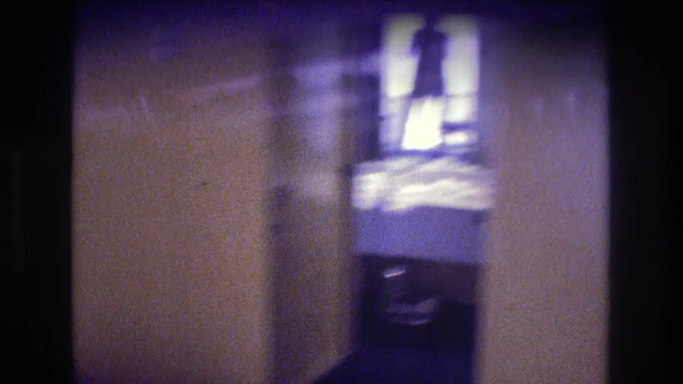 8mm home-movie mid-shot showing a tan hallway wall and a backlit adult silhouette standing in a bright rectangular opening, Acapulco circa 1982.