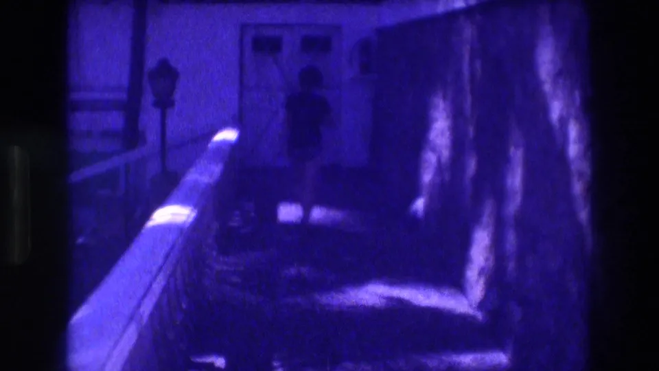 1982 Acapulco hotel balcony; strong purple-blue film aging; silhouetted figure walks along corridor railing with lamp post and palm trees in background.