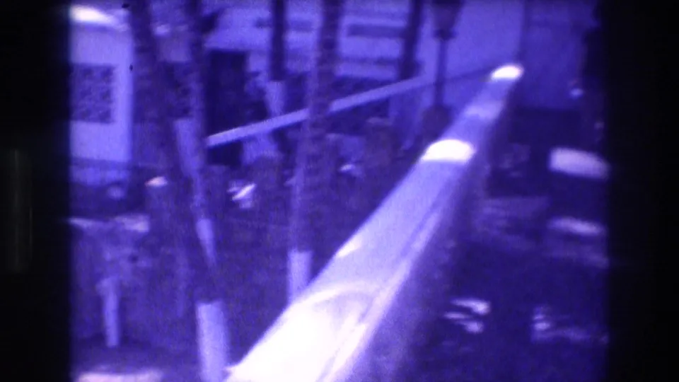 Hotel balcony railing and palm trees at 1982 Acapulco resort; pronounced blue-purple aging cast from 8mm film stock; building facade visible in background.