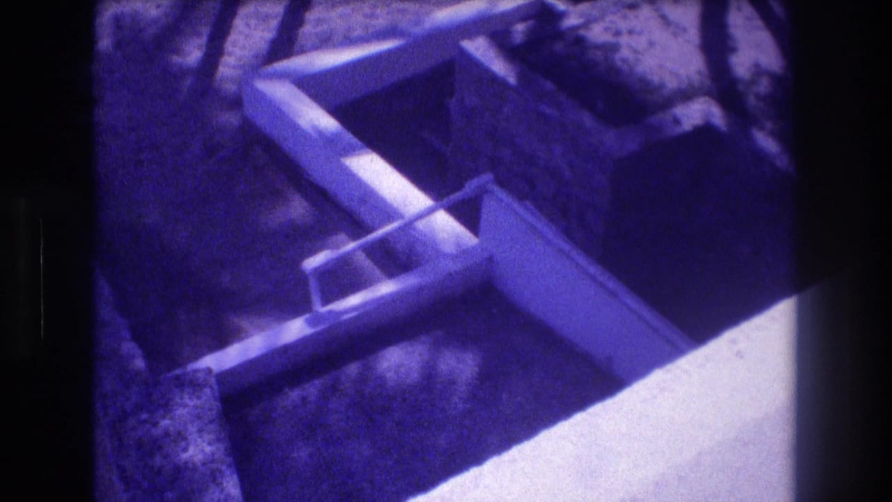 Concrete foundation forms seen from above at a 1982 Acapulco construction site; stepped formwork visible against sandy earth in aged 8mm footage with strong purple dye shift.