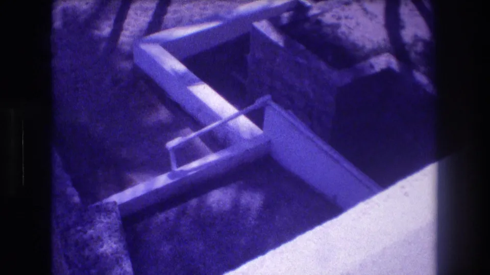 Concrete foundation forms seen from above at a 1982 Acapulco construction site; stepped formwork visible against sandy earth in aged 8mm footage with strong purple dye shift.