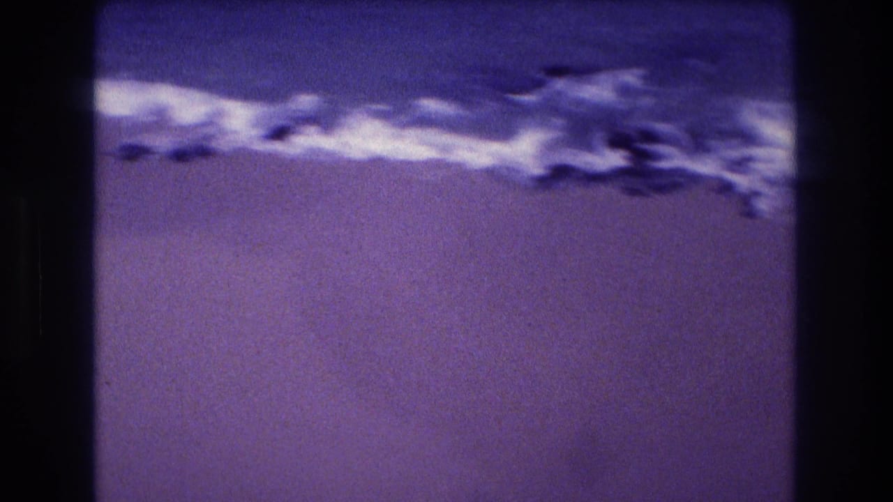 Wide shot of a flat sandy beach with foam-edged surf across the upper frame, strong purple color shift consistent with early-1980s 8mm film, Acapulco, Mexico.