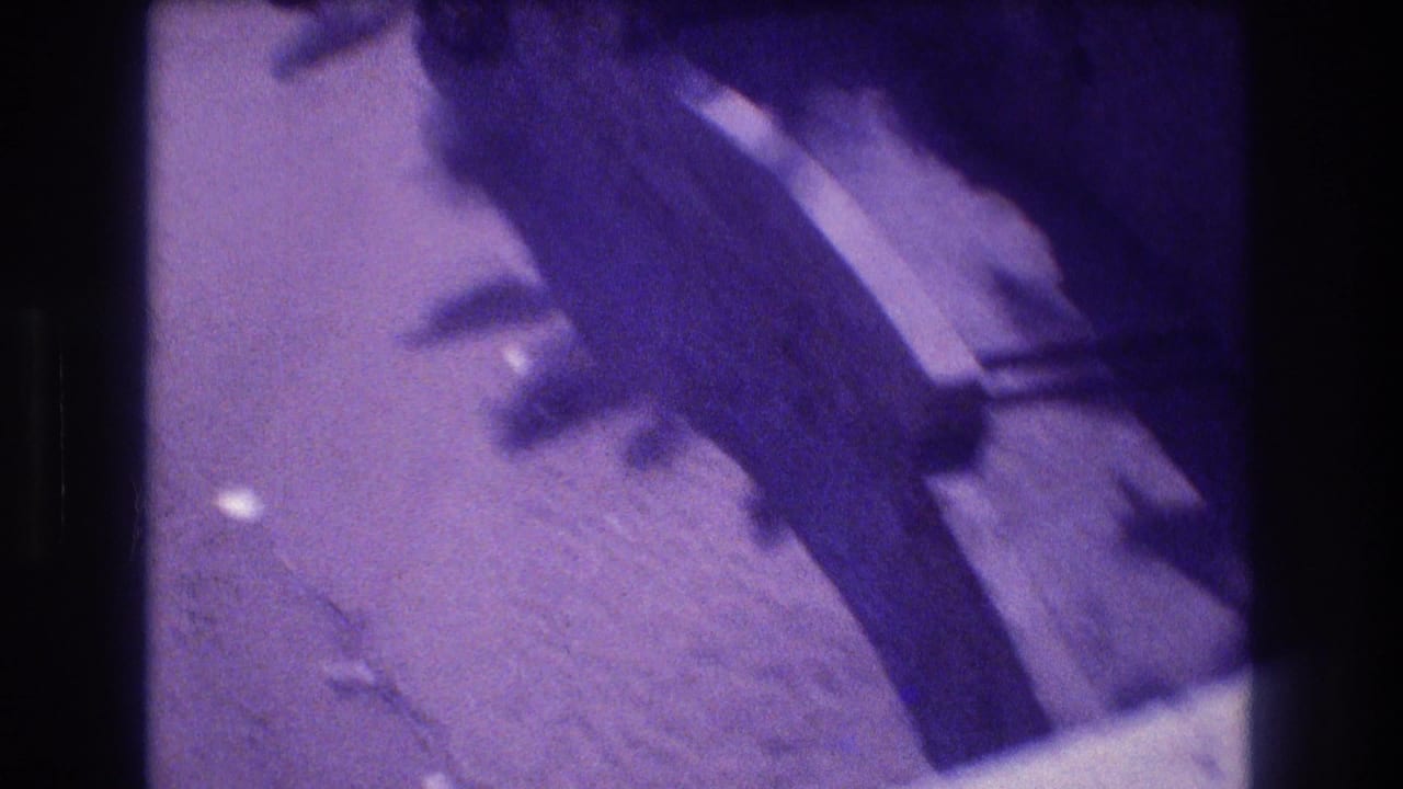 Heavily motion-blurred 8mm frame showing dark rock surface and sandy ground during a camera pan; strong purple dye-shift from aged film stock, Acapulco area, circa 1982.