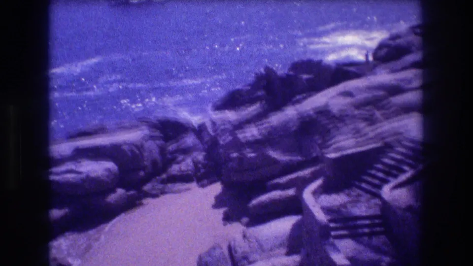 8mm home-movie frame showing a jagged rocky coastline with breaking waves and open ocean beyond; strong purple color cast from aged film emulsion, likely Acapulco, Mexico, circa 1982.
