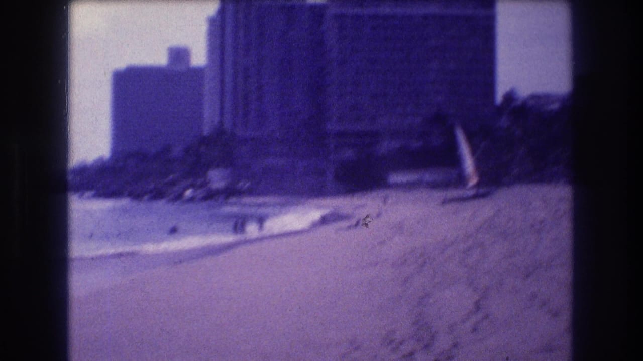 8mm home movie frame showing Acapulco beach c.1982 — surf approaching shore, a high-rise hotel tower at left, a possible windsurfer near the waterline, and overexposed sky.