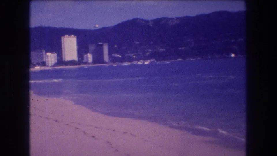 8mm home movie of Acapulco beach showing bay view with resort towers and mountains, circa 1982, nearly identical composition to the opening frame with continued purple color drift.
