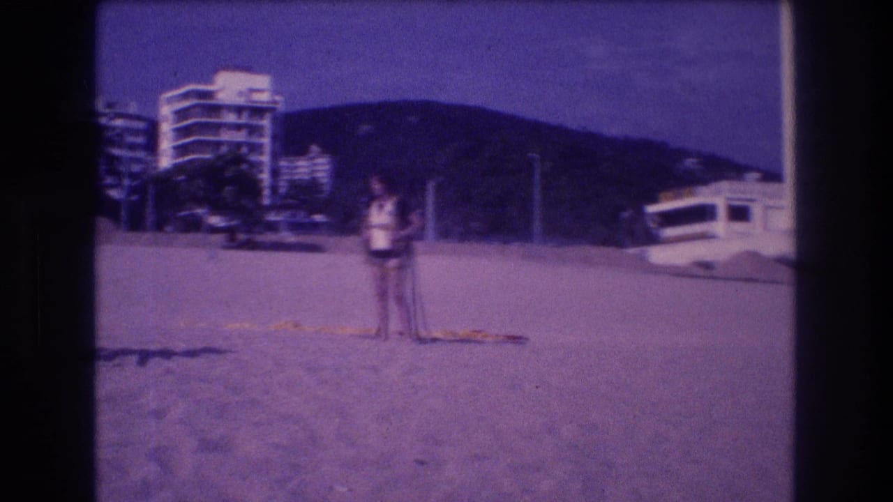 Adult figure on Acapulco beach circa 1982; multi-story hotels, a white vehicle at the hotel base, and green coastal hills visible behind.