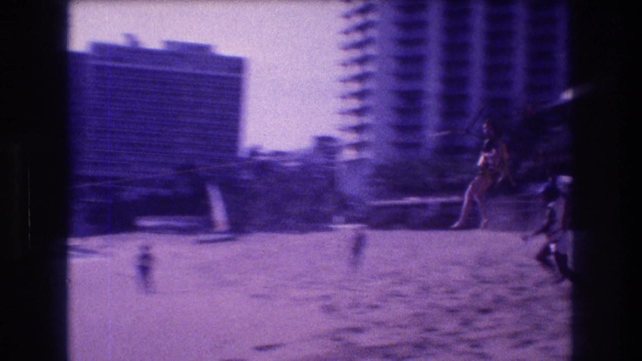 Motion-blurred closing frame from an Acapulco beach in 1982, showing hotel high-rises and scattered beachgoers as the camera completes its pan following the zip-line rider.