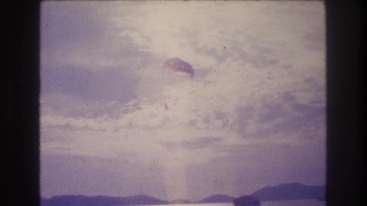8mm home-movie frame circa 1982 showing a parachute descending toward the horizon over what appears to be coastal water near Acapulco, Mexico.
