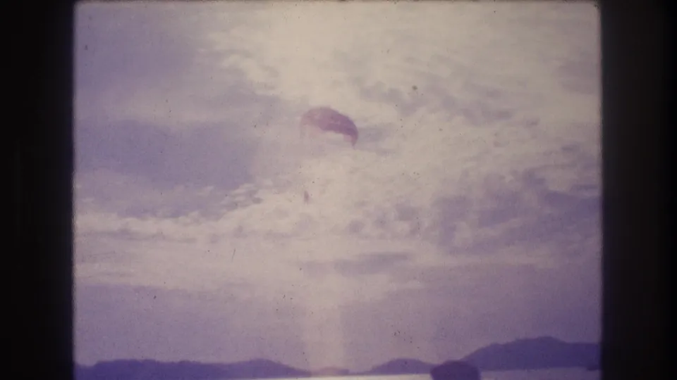 8mm home-movie frame circa 1982 showing a parachute descending toward the horizon over what appears to be coastal water near Acapulco, Mexico.