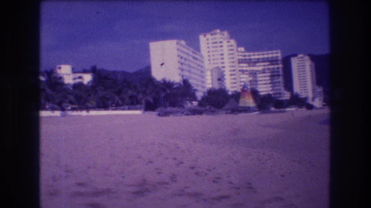 Sandy beach in foreground with white high-rise resort hotels and colorful conical palapas along the shoreline; pronounced purple film color cast.