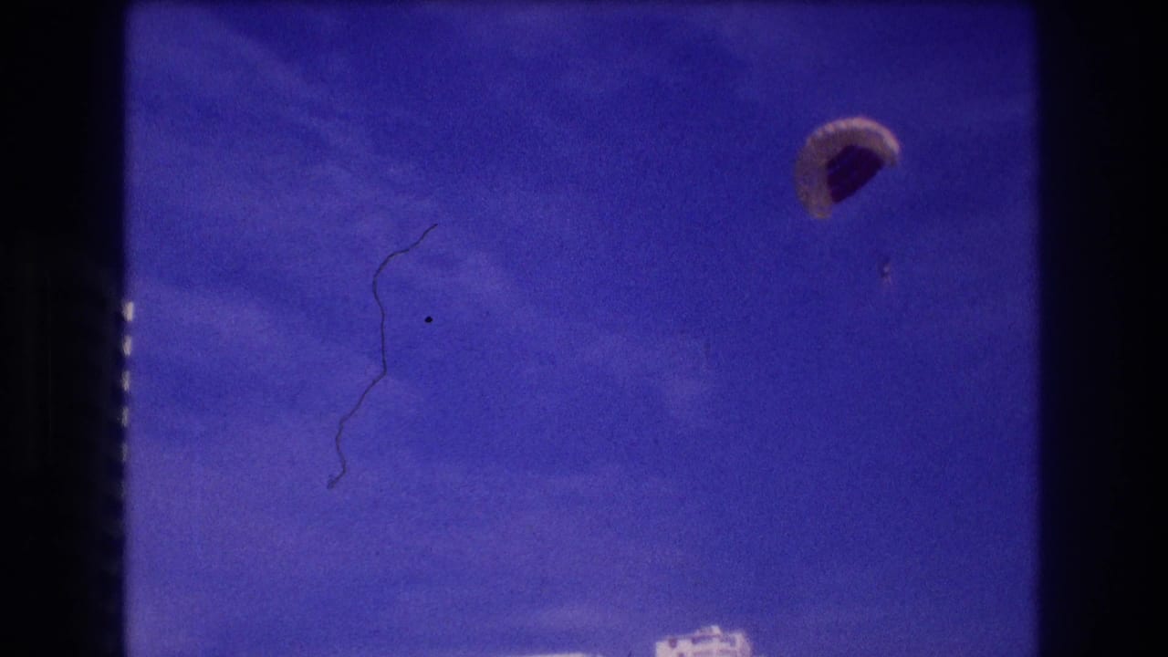 Opening 8mm frame from Acapulco, 1982 — parasail canopy drifts against deep blue sky with a film emulsion scratch artifact visible on the left.
