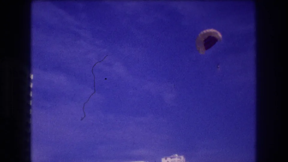 Opening 8mm frame from Acapulco, 1982 — parasail canopy drifts against deep blue sky with a film emulsion scratch artifact visible on the left.