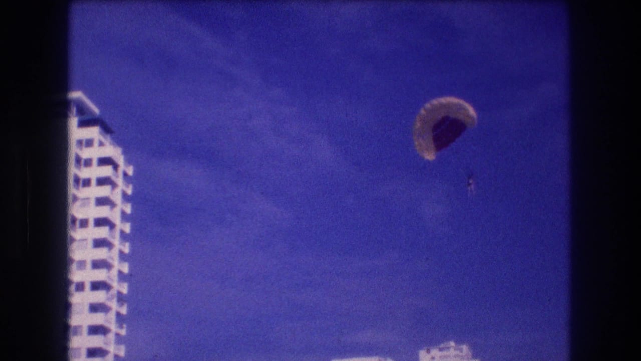 8mm home-movie frame from Acapulco, 1982 — white multi-story resort hotel fills left side as parasail canopy continues descent in upper right.