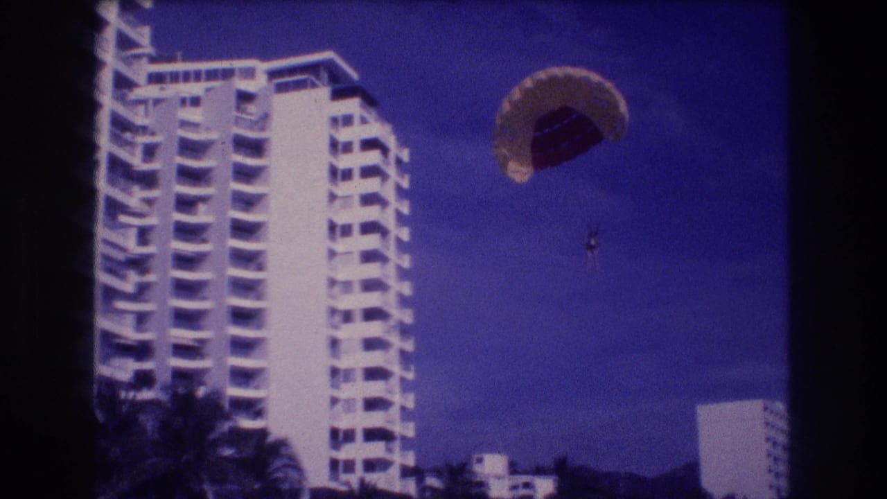 Super 8 home movie frame, c.1982 Acapulco: parasailor aloft above a beachfront high-rise hotel, palm trees visible at the base