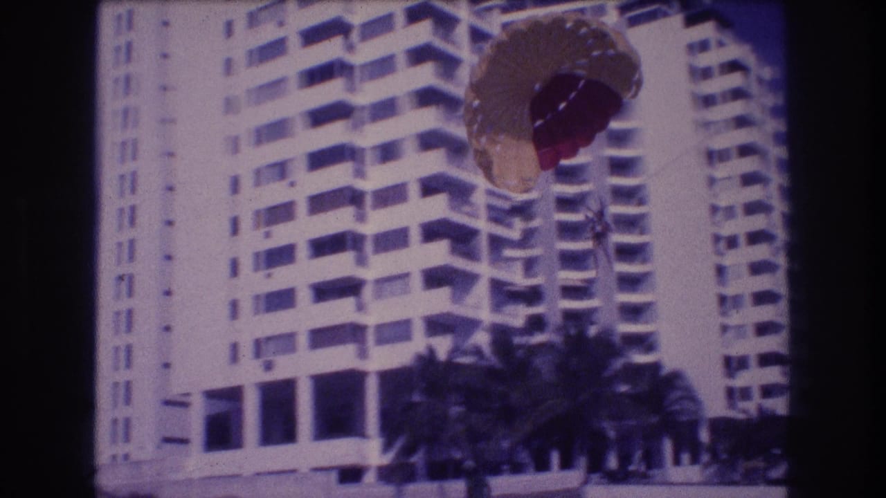 Super 8 home movie, c.1982 Acapulco: close view of parasail canopy with resort hotel and palm trees as parasailor nears the beach