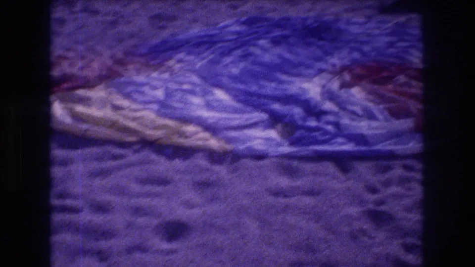 Ground-level close-up of a deflated parachute canopy on Acapulco beach sand, 1982; blue, red, and white fabric panels with visible 8mm grain and purple color cast.