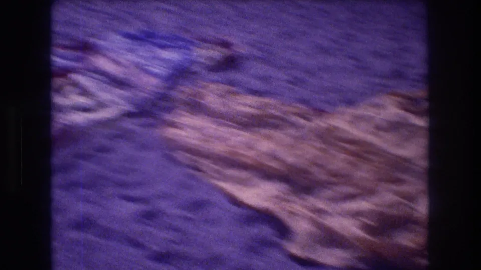 8mm close-up of a parachute canopy on Acapulco beach sand, 1982; blue and orange fabric panels caught mid-motion with film grain and purple color cast.