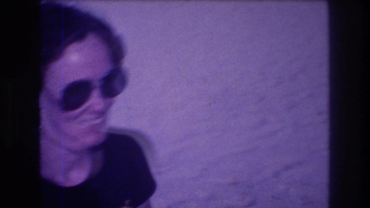 Cropped close-up of a woman in large 1980s-style sunglasses, from an 8mm home movie filmed in Acapulco, Mexico, circa 1982; pronounced purple color cast.