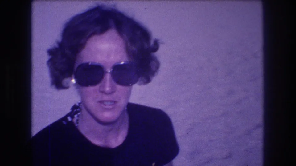 Woman in large-frame sunglasses and patterned necklace speaking to the camera operator, from an 8mm home movie filmed in Acapulco, Mexico, circa 1982.