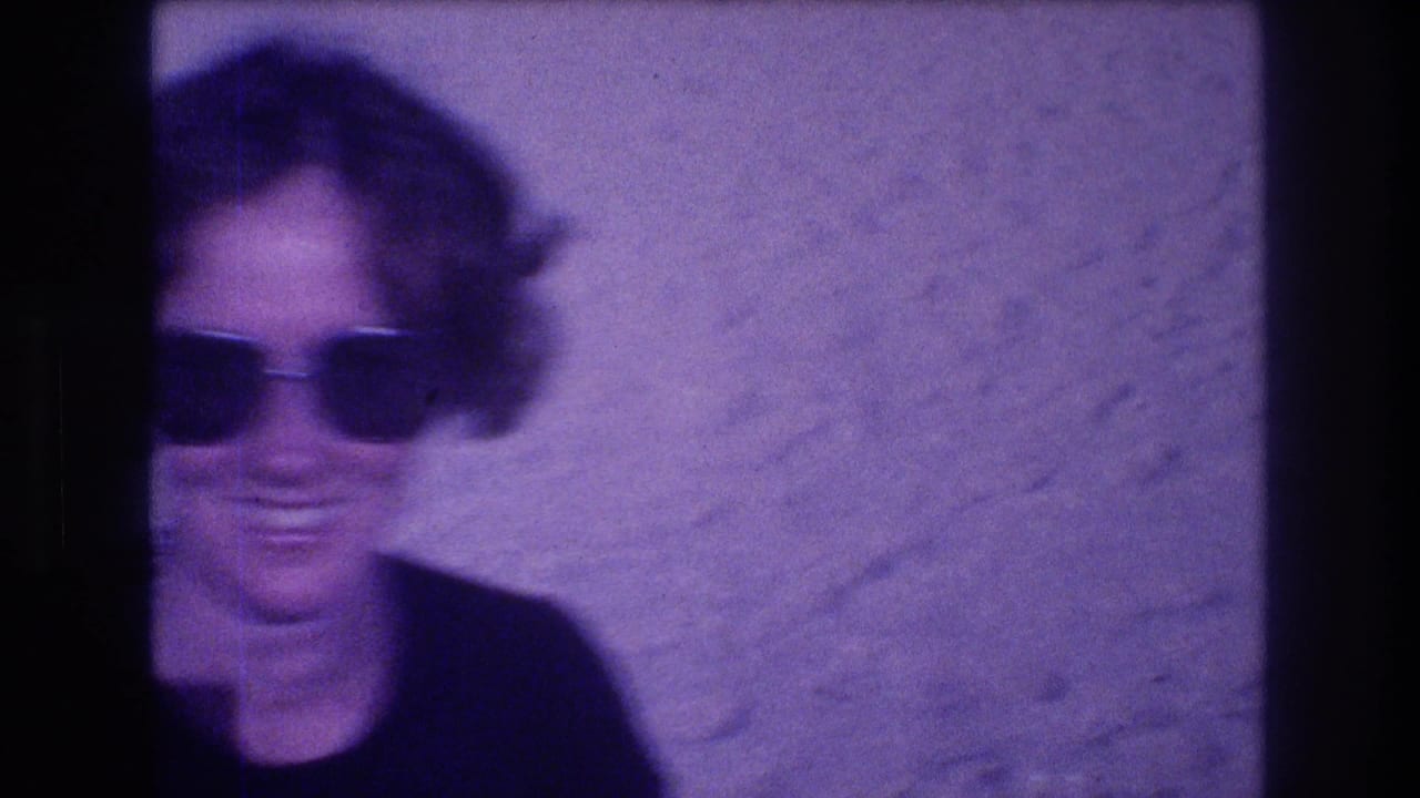 Woman with oversized dark sunglasses smiling as camera begins to pan away, motion blur visible, Acapulco Mexico circa 1982, 8mm film.