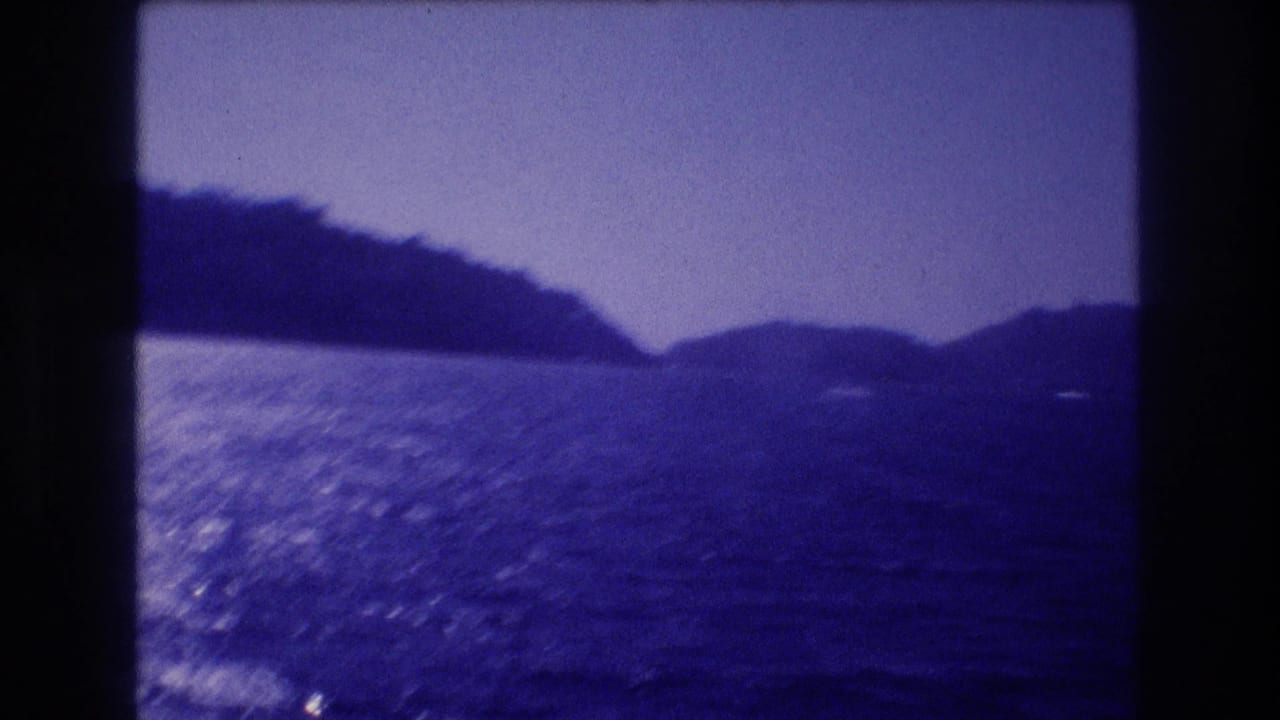 Dark choppy seawater with light glare, dark mountain ridge above, pale sky, strong blue film cast.