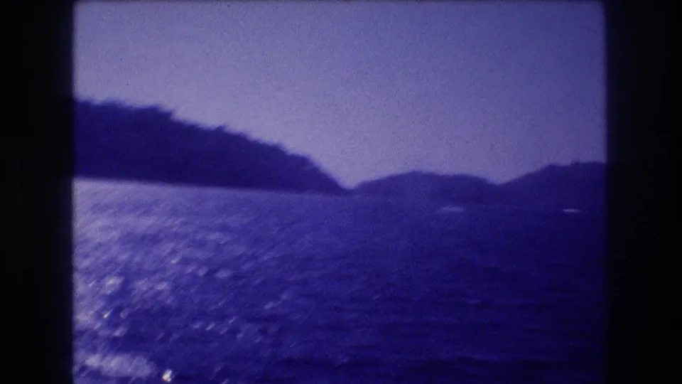 8mm home-movie frame from approximately 1982 showing choppy coastal water with sunlight glare, a dark mountain ridge, and aged blue emulsion cast, likely Acapulco, Mexico.