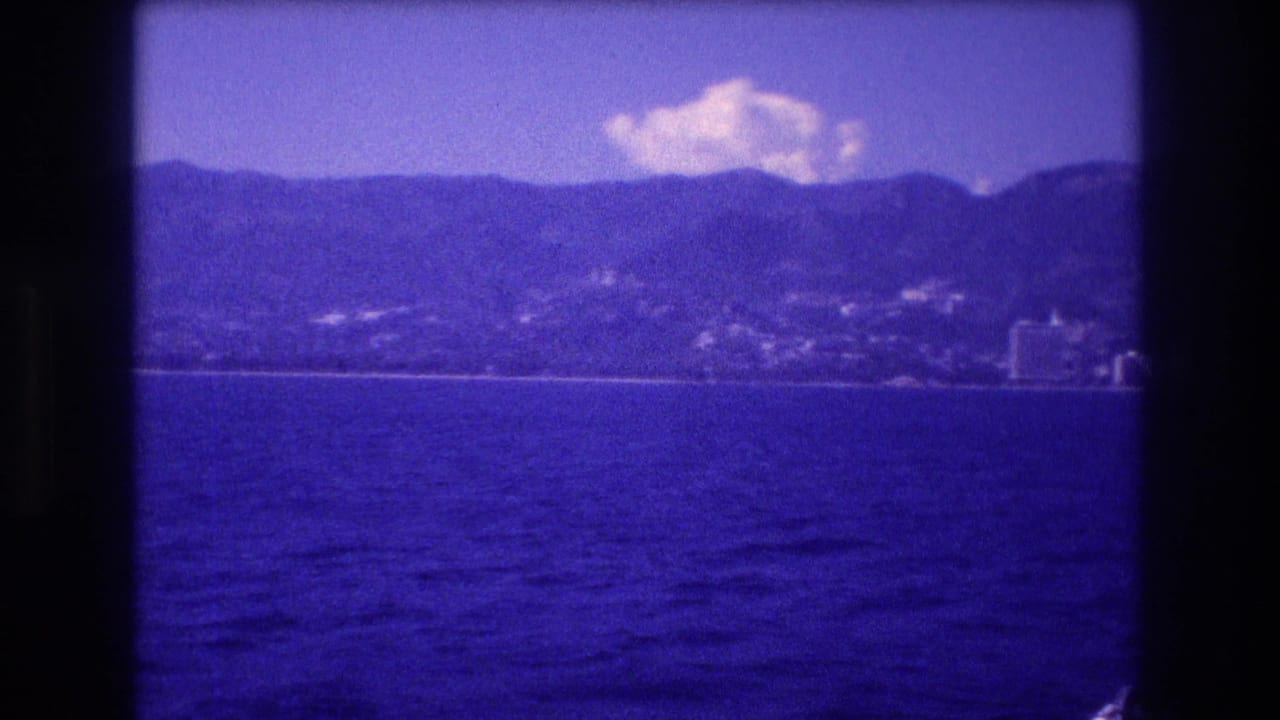 8mm home movie frame from Acapulco bay, 1982 — hotel zone skyline with backing mountain range, shot from a moving boat with heavy blue color cast