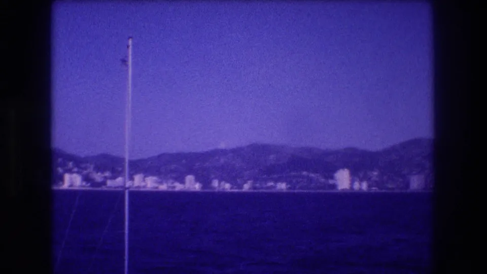 8mm home movie, circa 1982, boat-POV of Acapulco resort coastline with mast and mountain ridge, heavy blue film shift