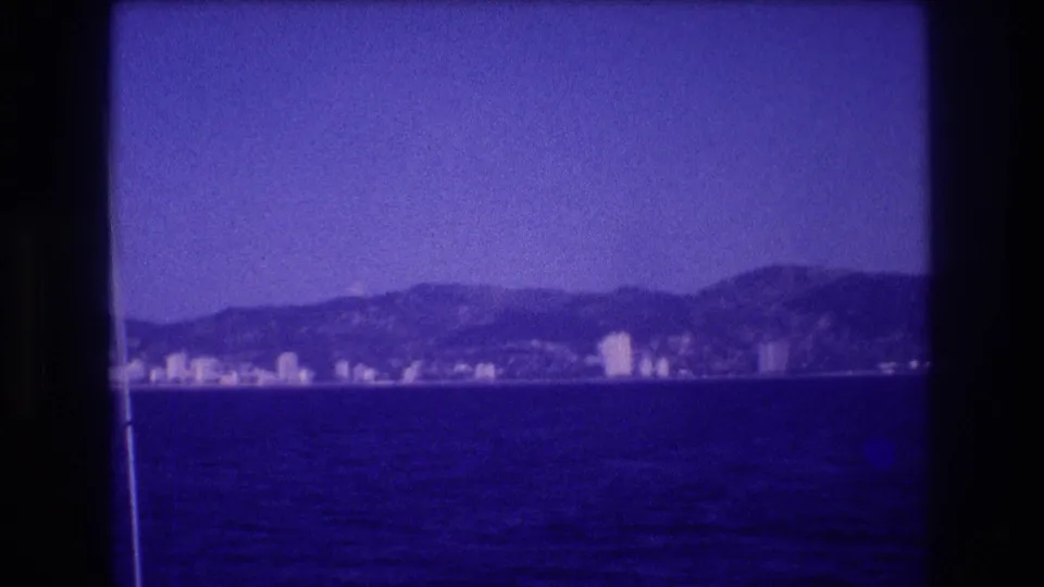 8mm home movie, circa 1982, Acapulco coastal strip seen from water, high-rise cluster at right with mountain backdrop, blue dye cast