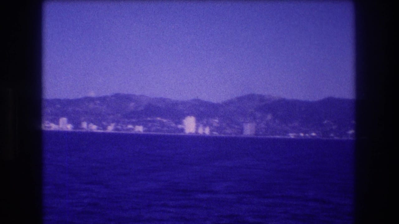 Calm open water stretching toward a low coastal skyline with rolling hills and a cluster of white mid-rise buildings.