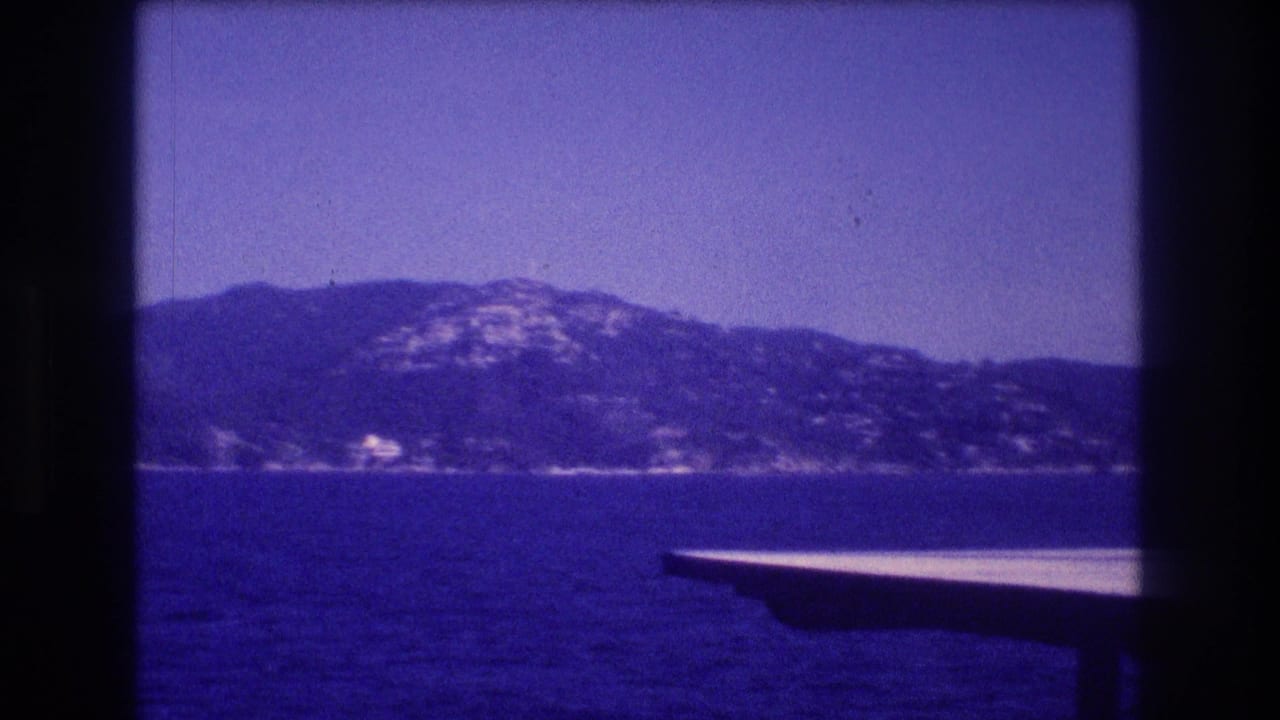 Blue-tinted 8mm frame from the supplied 1982 Acapulco footage showing open water, a hazy mountain shoreline, and the edge of a boat in the foreground.