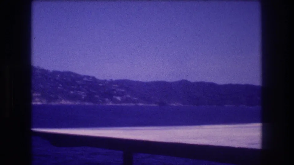 Blue-purple 8mm view from a boat near Acapulco, with distant hills and shoreline across calm water under a clear sky.