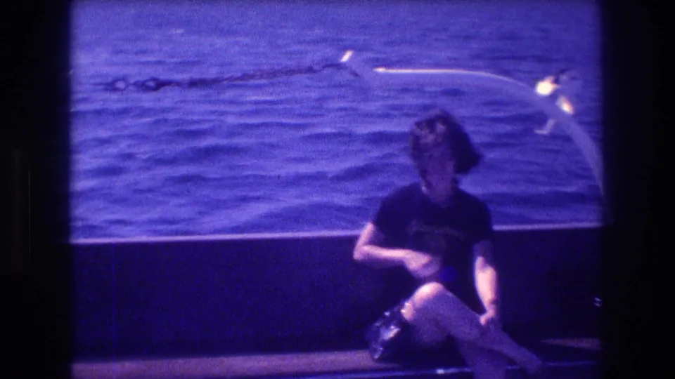 The woman remains seated on the boat in Acapulco, looking downward near a white curved rail with rippled sea in the background.