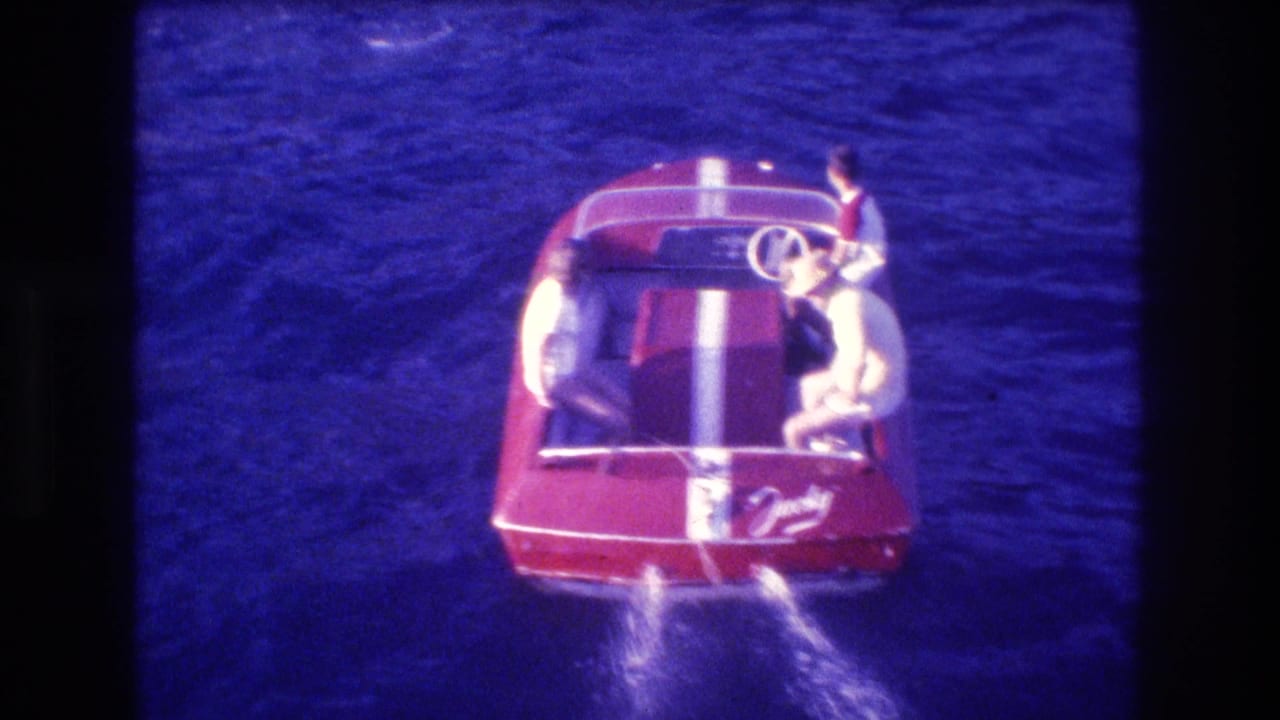 Red boat seen from above with passengers and wake behind it.