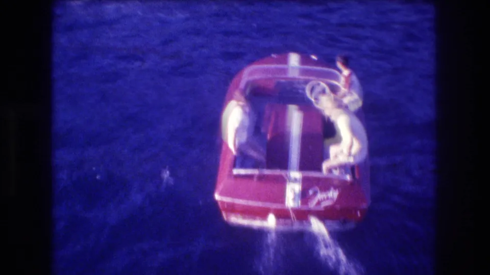Overhead 1982 Acapulco home-movie still of a red speedboat crossing blue water, with one person at the controls and others gathered near the rear seats.