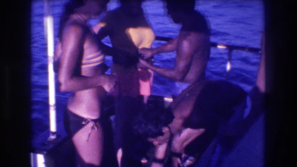 In this 1982 Acapulco home-movie frame, adults in swimwear gather on a small boat beside a white pole, with blue water behind them and a strong purple-blue film cast.