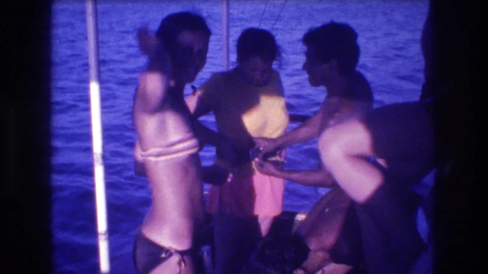A woman in a bikini and two nearby men in swimwear stand closely on a boat during a 1982 Acapulco outing, framed by water and aged 8mm color shift.