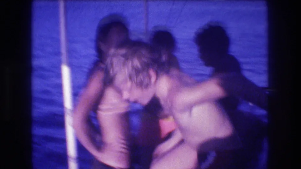 A soft, motion-blurred 8mm frame shows people in swimwear leaning and standing together on a boat in Acapulco, with open water behind them and heavy blue-purple color shift.