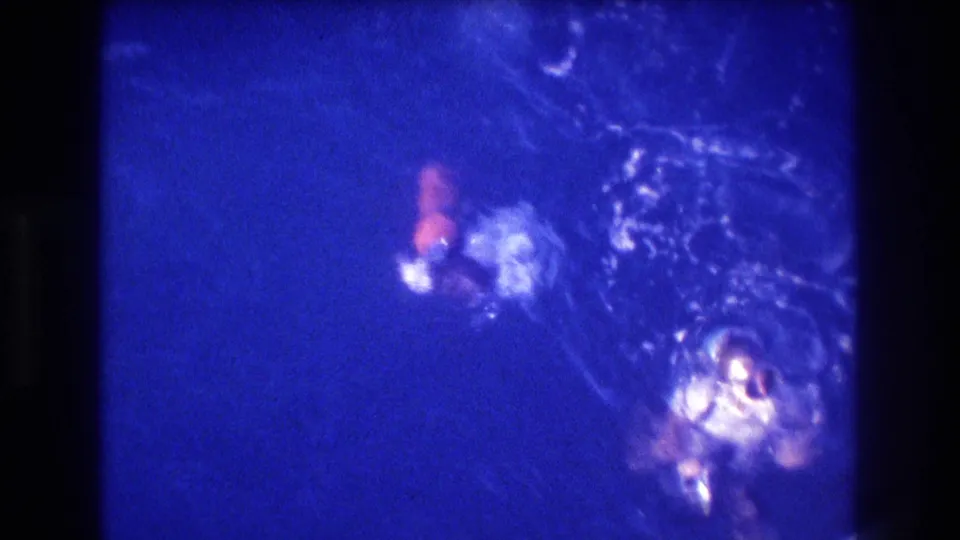 Overhead 8mm view of swimmers in deep blue ocean water, with bright bubbles and surface disturbance suggesting snorkeling or swimming activity.