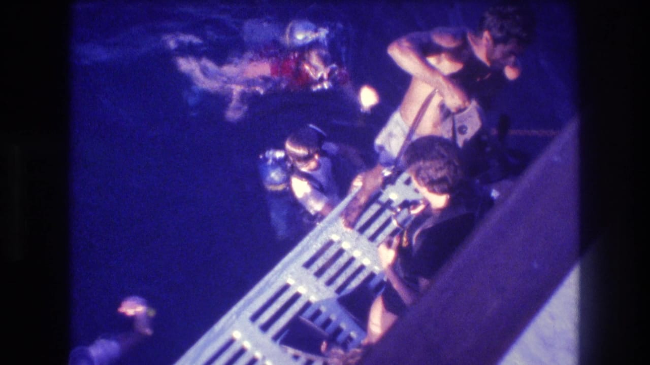Overhead 8mm shot from a dive boat circa 1982, showing a small group near a metal boat railing and ladder over deep blue ocean water.