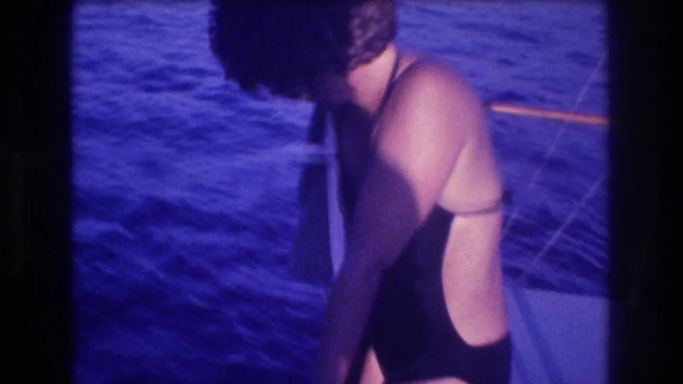 8mm shot of a woman in a dark swimsuit leaning over a dive boat deck, looking down at deep blue ocean water, Acapulco Mexico circa 1982.
