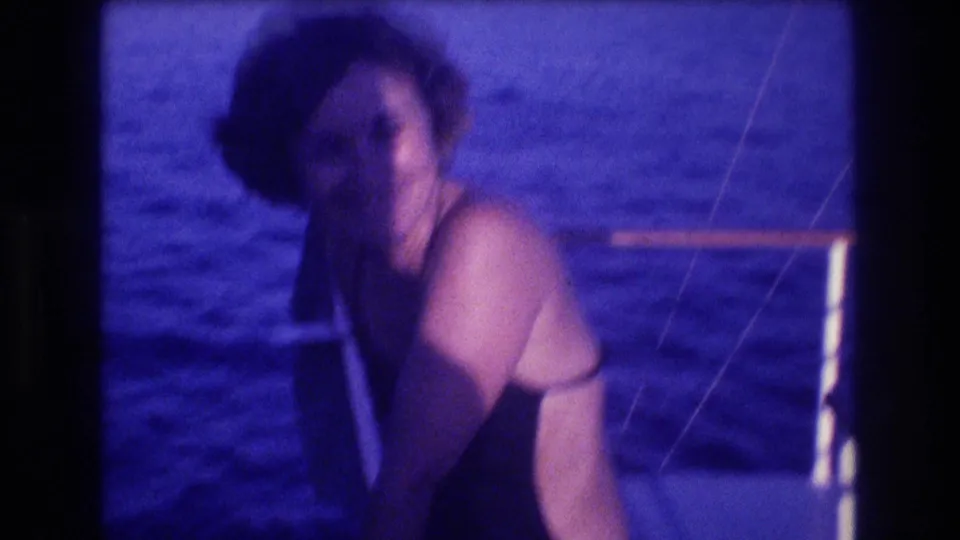 Same woman turning slightly away from the camera on a boat deck, boat rigging at frame right, blue ocean behind, 8mm home movie, Acapulco, Mexico, circa 1982.