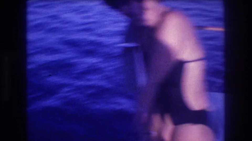 Motion-blurred frame of woman in dark swimsuit bending or moving on boat deck, orange rope railing visible, 8mm home movie, Acapulco, Mexico, circa 1982.