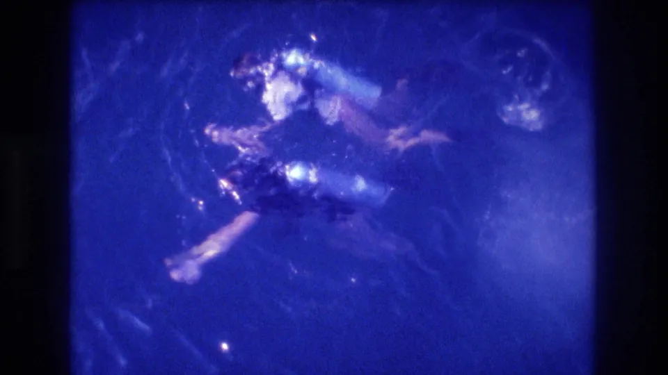 Two scuba-equipped figures filmed from above in deeply blue-shifted ocean water; consistent with 1982 8mm home-movie footage per clip metadata indicating Acapulco, Mexico.