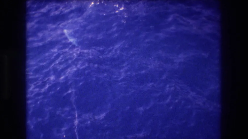 Super 8 home-movie shot of open ocean surface showing wave ripples and a faint pale shape beneath the water, possibly Acapulco 1982.