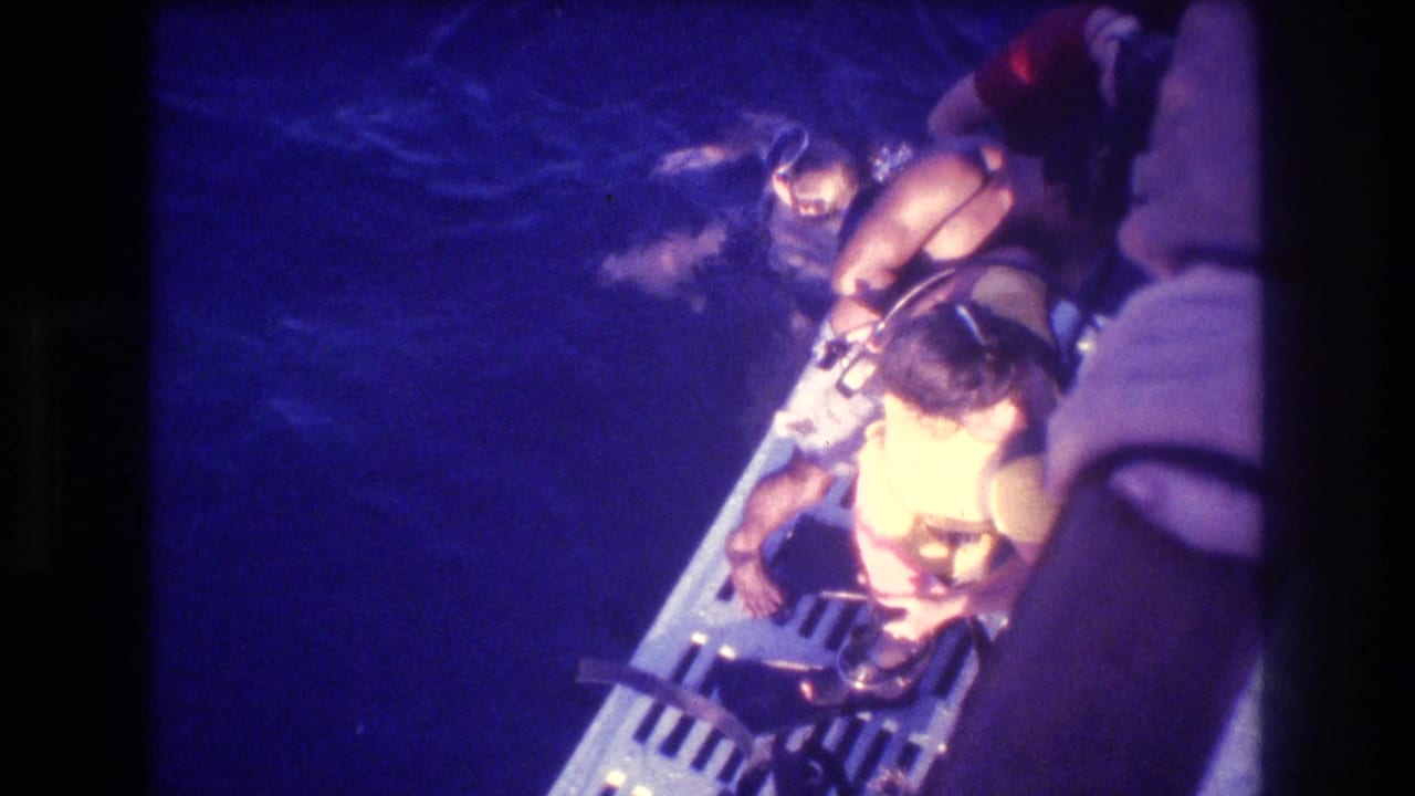 Overhead view of a child in a yellow life vest on a boat boarding platform at night, Acapulco, Mexico, circa 1982, shot on 8mm home movie film.